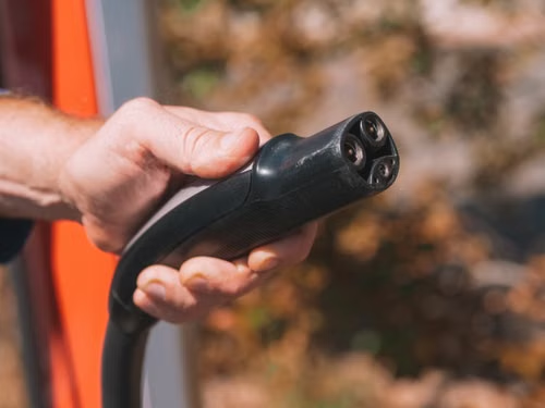 person-holding-charger A person holds an EV charger port in their hand.